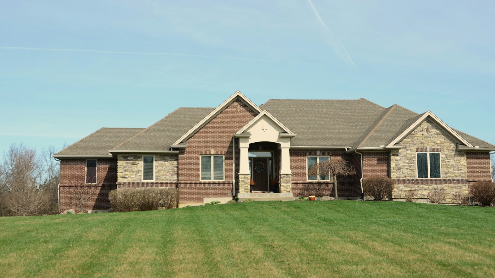 A brick and stone home with a broad mown front lawn in late fall, the kind of maintained turf where vole runways turn up once the grass thins out